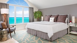 Hotelkamer met een groot bed, uitzicht op de oceaan, een bureau met een lamp en een stoel.