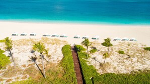Luchtbeeld van een strand met een pad naar strandstoelen en parasols.