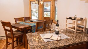 A dining area with a wooden table, chairs, a wine bottle, and glasses on a granite countertop. - Davis, WV 2BR full kitchen NR Stumptown Ales (Davis)