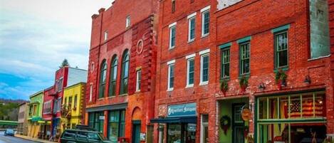 A street with red brick buildings, a green SUV parked on the side, and storefronts with various signs.