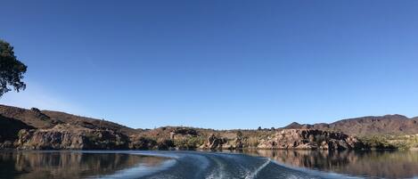 Vista despejada de un lago con estela tras un barco en movimiento, rodeado de colinas rocosas y vegetación escasa.