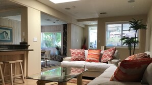 A living room with a glass coffee table, a white sofa with patterned cushions, and a kitchen area with a bar counter and stools. - Private Marina, Docks, Close to Golf Course, Restaurants. (Parker)