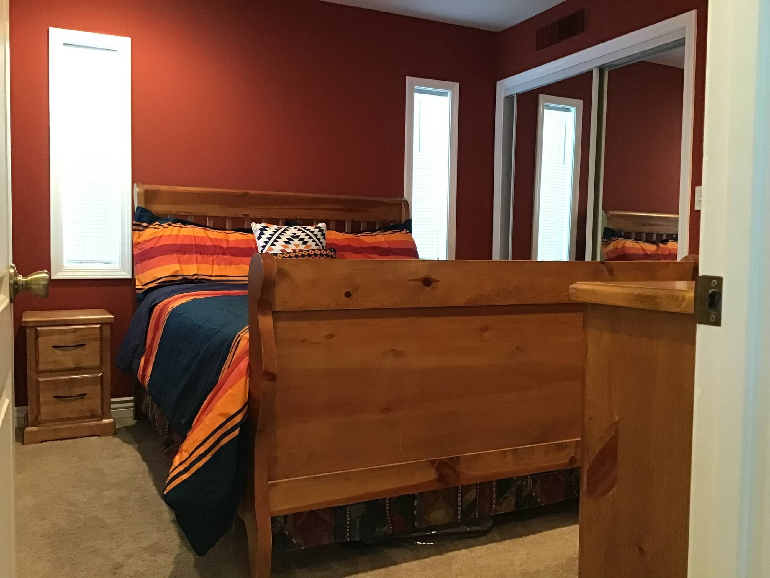 A bedroom with a wooden bed, a nightstand, a dresser, and a mirror.
