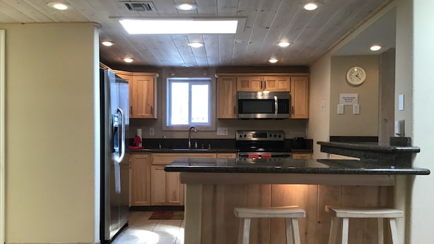 A kitchen with wooden cabinets, a stainless steel refrigerator, a microwave, an oven, and a sink. There are two stools at the island. - Private Marina, Docks, Close to Golf Course, Restaurants. (Parker)
