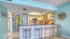 Una cocina moderna con una isla central, taburetes de bar y un reloj decorativo.