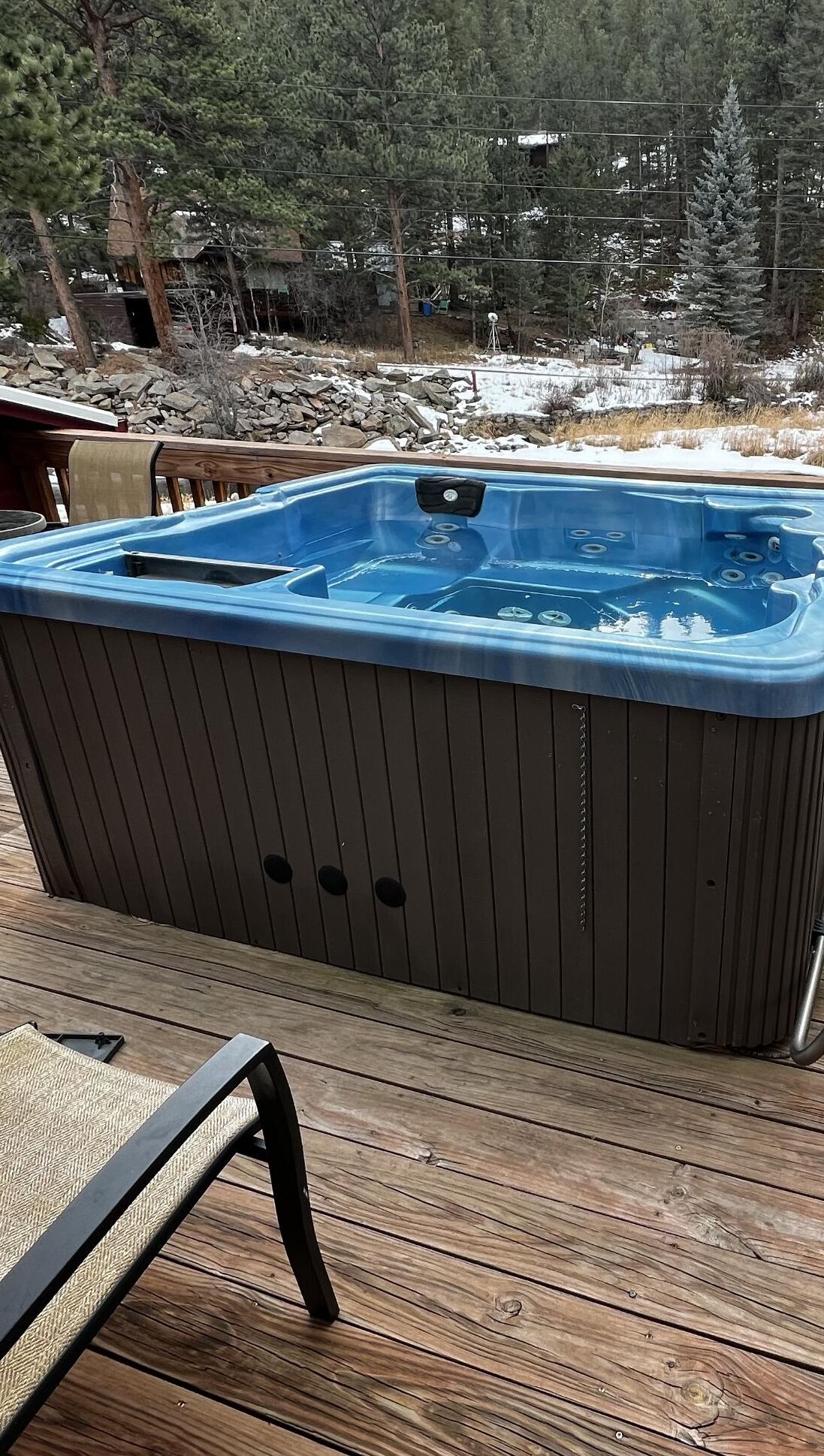 A hot tub on a wooden deck with a view of a snowy landscape and trees.