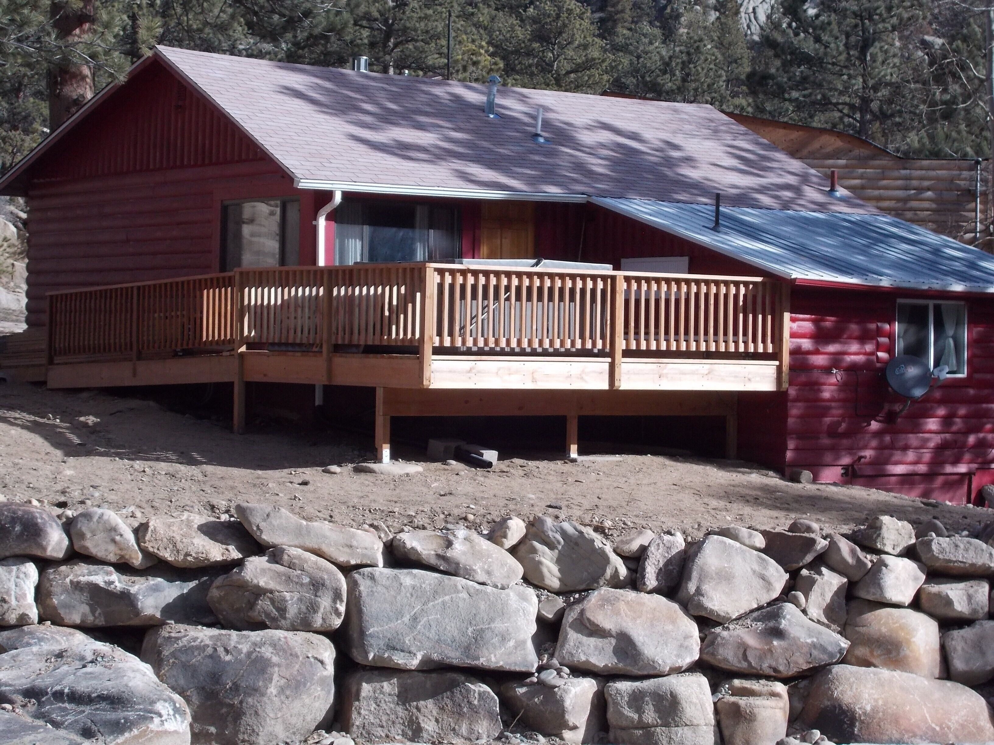 Une cabane dotée d’une terrasse en bois et d’un mur en pierre à l’avant.