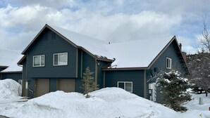 Une maison à deux étages, à l’extérieur d’un bleu foncé, avec un garage et une allée recouverte de neige.