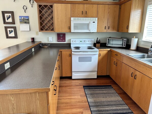 A compact kitchen with wooden cabinets, a white stove, a microwave, and a toaster. - The BEST Deal!! Spacious Well Appointed Condo with Private Hot Tub (Big Sky)