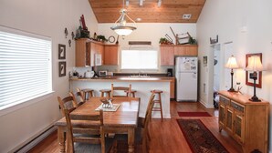 Une cuisine avec des meubles de rangement en bois, une table à manger avec des chaises, un réfrigérateur et un luminaire suspendu.
