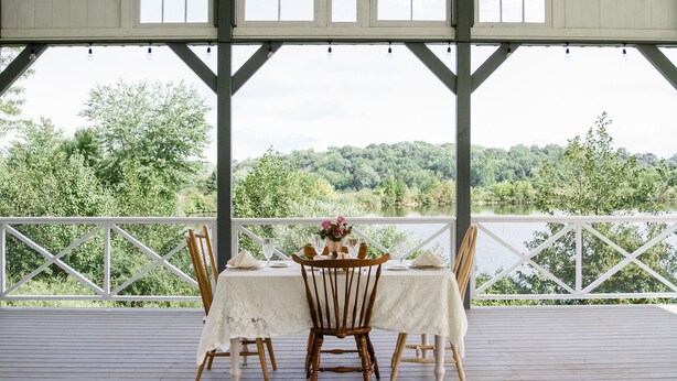 Un espace de restauration en plein air avec une table dressée pour quatre personnes, offrant une vue sur un lac et une zone boisée.