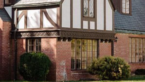 Une maison de style Tudor, dotée d’un toit à forte pente, de poutres apparentes et d’une cheminée en briques.