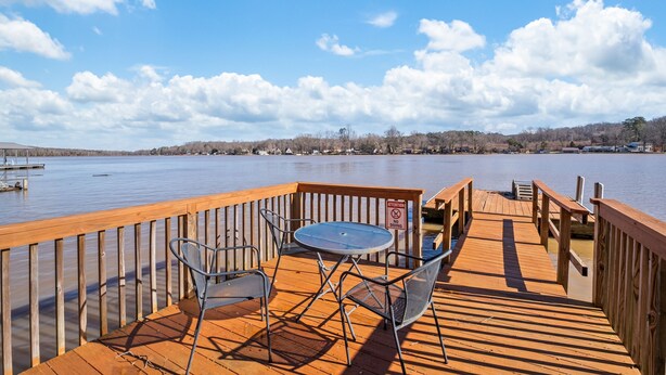 Une terrasse en bois avec une table et des chaises donnant sur un lac paisible.