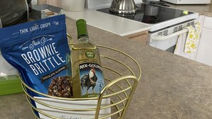 Un comptoir de cuisine avec un sachet de « Brownie Brittle » de Sheila, une bouteille de Rex-Gollie Pinot G et un panier en métal.