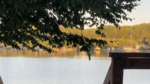 Une terrasse en bois surplombe un lac paisible, avec un quai et un chien allongé sur la terrasse.