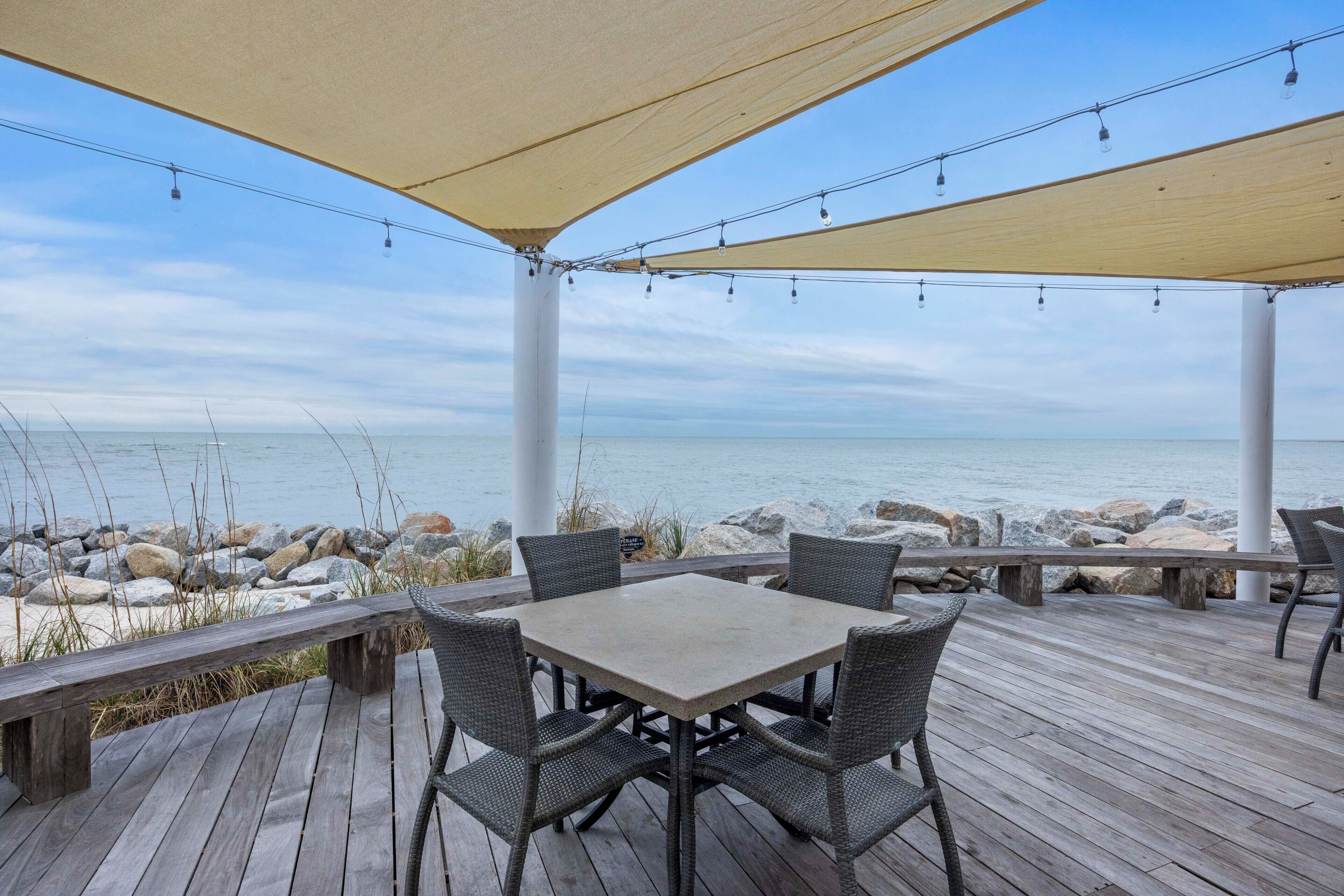 A covered outdoor seating area with a table and chairs, overlooking a rocky shoreline.