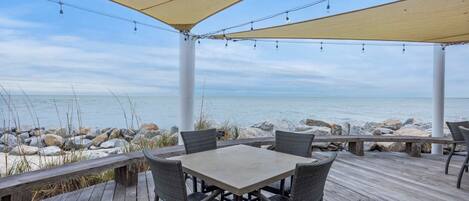A covered outdoor seating area with a table and chairs, overlooking a rocky shoreline.