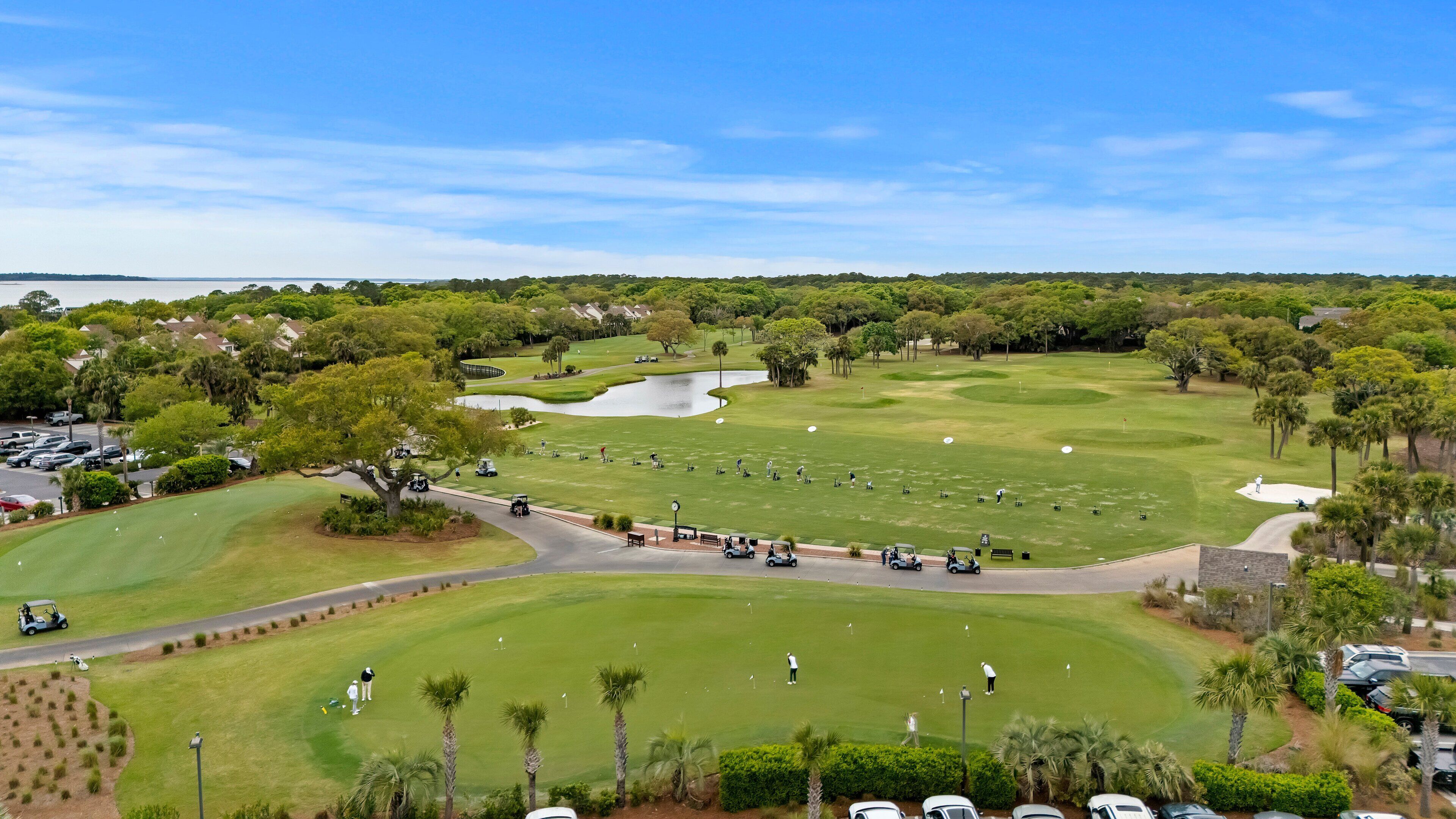 Campo de golf con un estanque, palmeras y un área de estacionamiento.