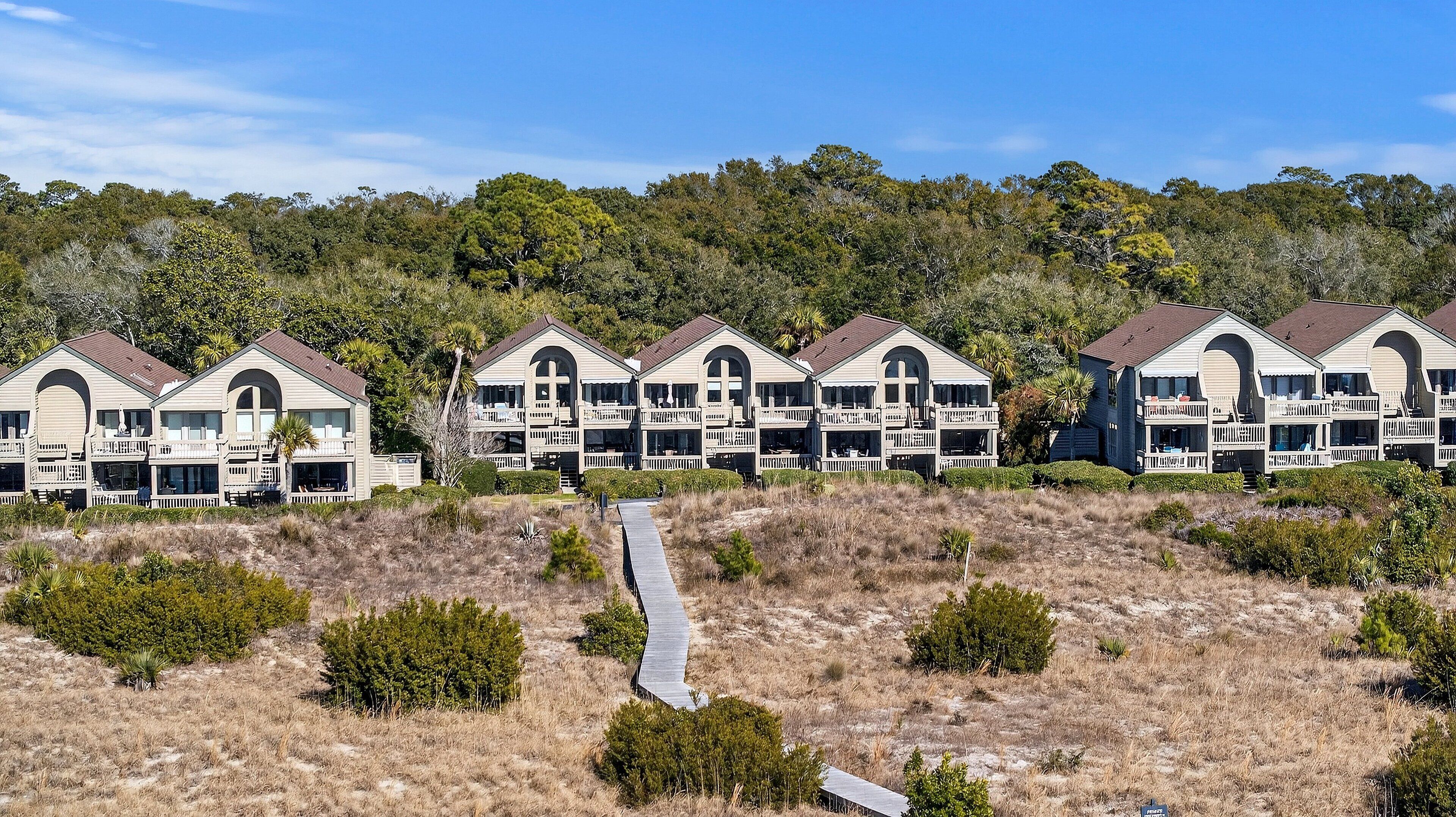 A row of beachfront cabins with multiple balconies, a central walkway, and a backdrop of dense forest.