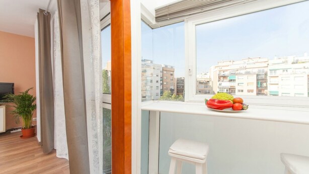 Un balcón con vistas a edificios de la ciudad, una mesa pequeña con frutas y una planta en maceta.
