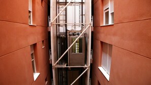 Un estrecho pasillo con andamios metálicos y paneles eléctricos, flanqueado por edificios con marcos de ventanas blancos.