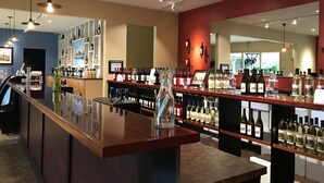 Una zona de bar con una barra larga, estantes con botellas y un espejo que refleja el interior.