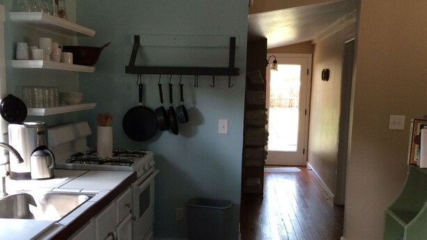 A kitchen with white cabinets, a stove, and hanging pots. There is a trash can and a patterned rug on the floor.
