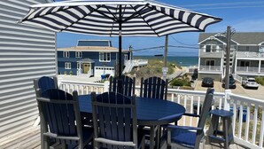 Un terrazza in legno con un tavolo rotondo e sedie, un ombrellone e vista sulla spiaggia e sull'oceano.