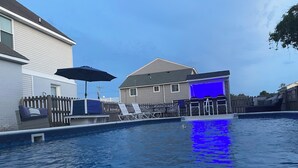 Una piscina con lettini e un ombrellone, circondata da una recinzione di legno e case.