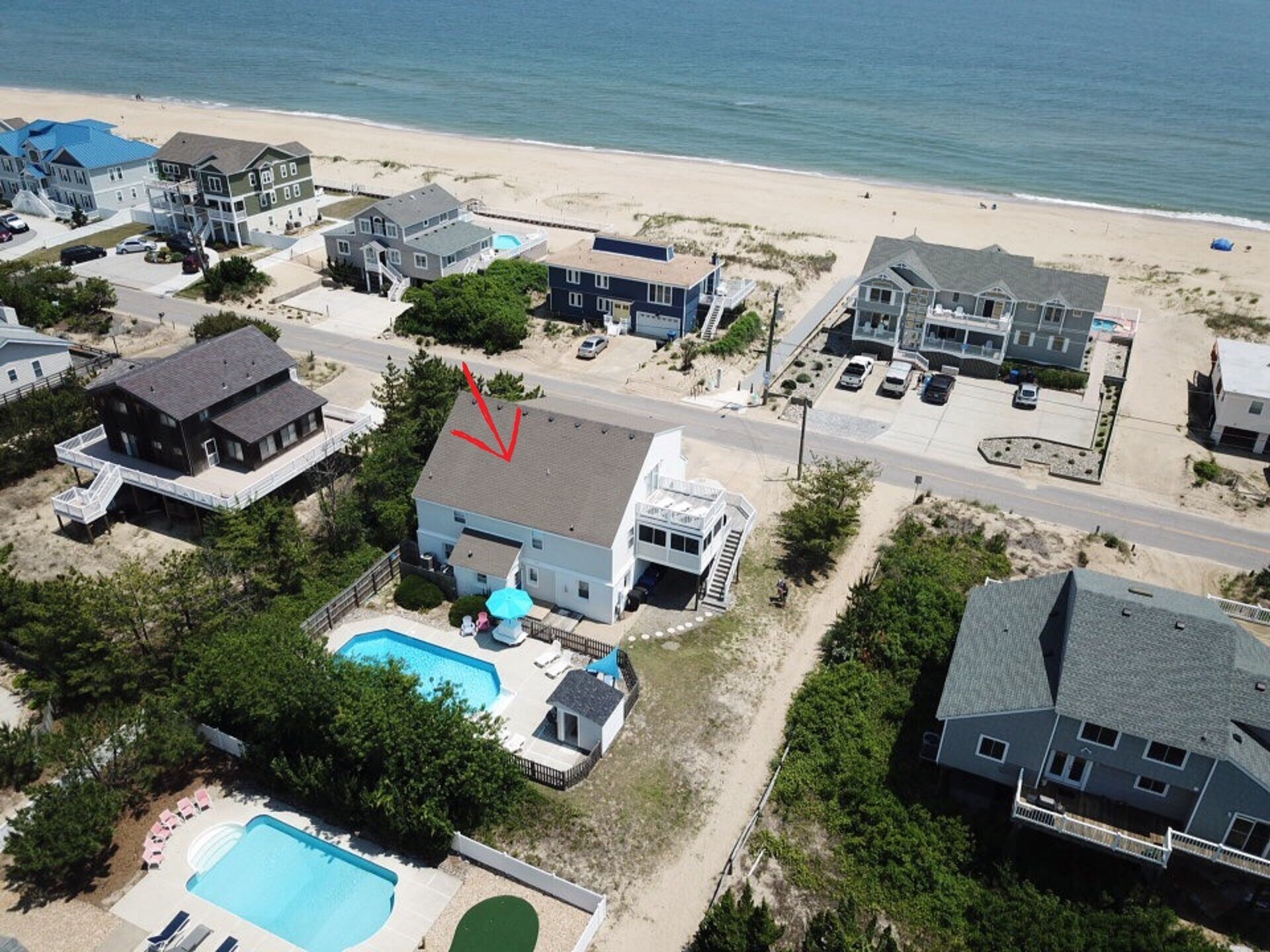 Vue aérienne d’un quartier résidentiel situé sur la côte, avec des maisons, une piscine et une plage.