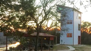 Un edificio con fachada blanca y detalles rojos, un área de picnic cubierta con bancos y un camino pavimentado.