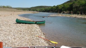 Orilla de río con un canoa verde y una remo en la orilla.