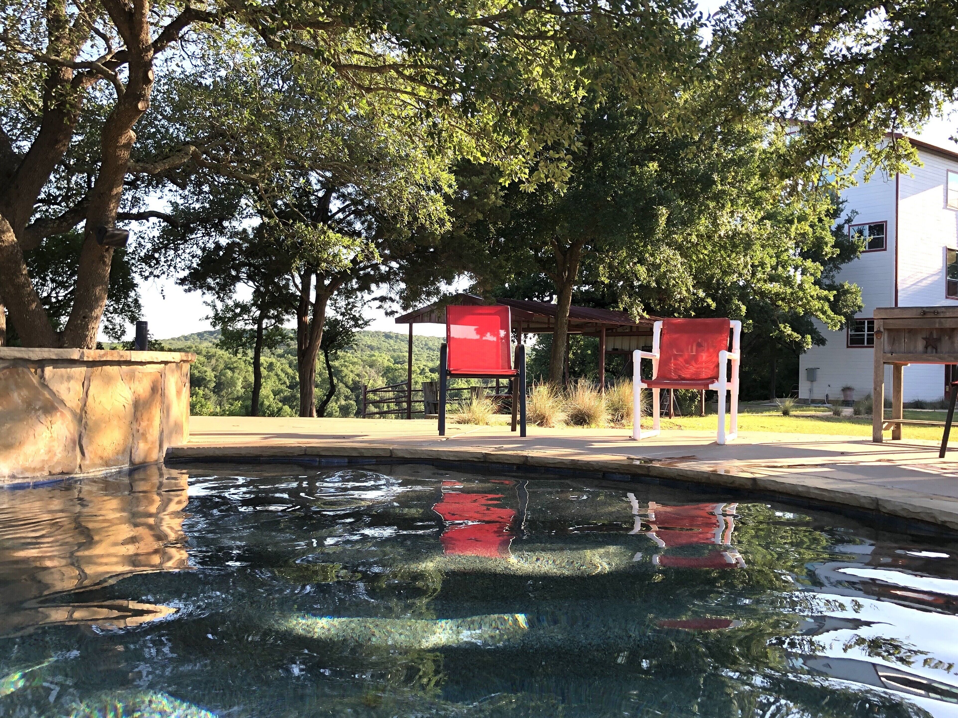 A swimming pool with clear water, surrounded by trees and a building in the background.