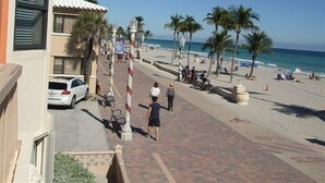 Ein Promenadweg am Strand mit Palmen, einem geparkten Auto und einer Person, die spazieren geht.