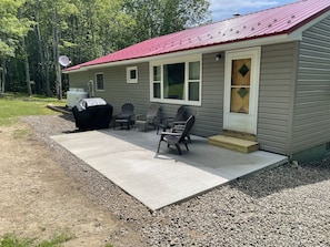 Un petit bâtiment d’un seul étage, avec un toit rouge, un espace extérieur abrité avec des chaises et un barbecue.