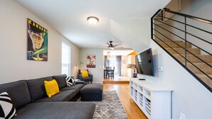 Ein modernes Wohnzimmer mit einem grauen Ecksofa, einer weißen Unterhaltungsecke und einer Treppe.