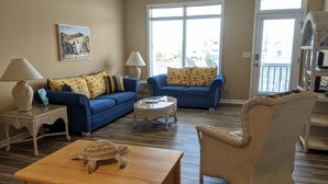 A living room with two blue sofas, a wicker chair, a wooden coffee table, and a small side table with a lamp. - On Sunset Beach Island 1 Bedroom Condo sleeps 4 Water view! Unit 2 (Sunset Beach)