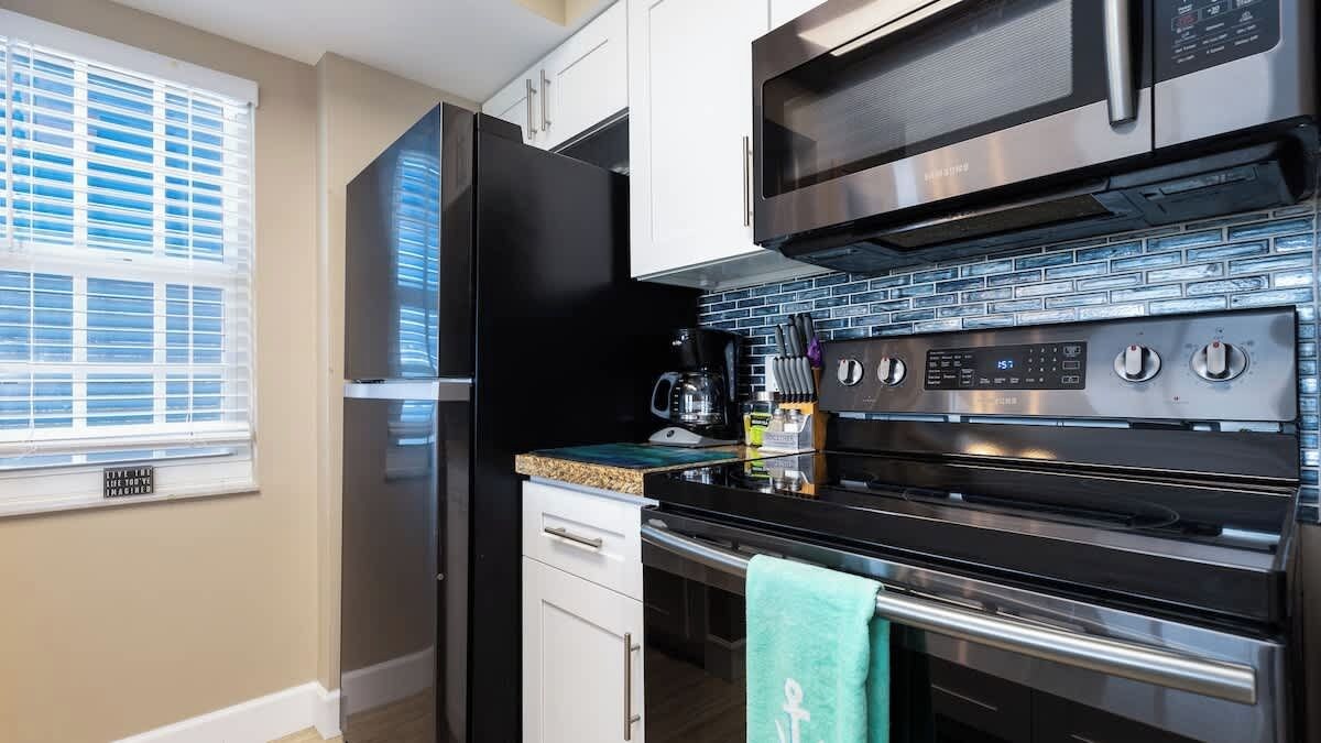 A modern kitchen with stainless steel appliances, a coffee maker, and a tiled backsplash.