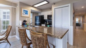 A modern kitchen with a granite countertop, stainless steel appliances, and wicker chairs.