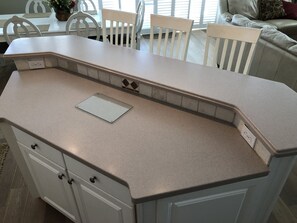 A kitchen with a white countertop, a small whiteboard, and a tiled backsplash.