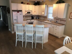 A modern kitchen with white cabinets, a central island with bar stools, a microwave, stove, and a refrigerator.