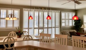 A dining area with a table and chairs, a ceiling fan, and large windows with blinds.