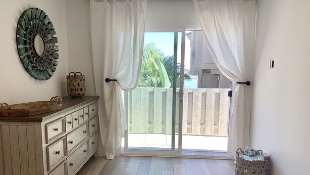 Een slaapkamer met een bed, een dressoir, een spiegel en uitzicht op een balkon.