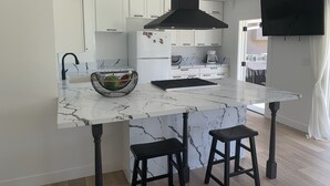 Een moderne keuken met witte kasten, een zwarte afzuigkap, een marmeren aanrecht en twee zwarte barkrukken.