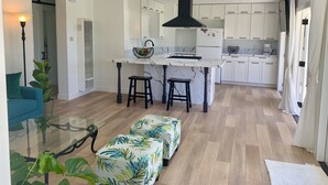 Een moderne keuken met witte kastjes, een zwarte afzuigkap en een marmeren aanrecht. Een barstoel en een plant staan op de voorgrond.