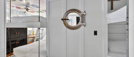 Une pièce avec des lits superposés, une porte blanche et un ventilateur de plafond.