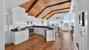 Een ruime keuken met witte kasten, een houten plafond en uitzicht op zee.