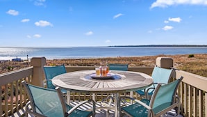 Een ronde houten tafel met stoelen op een terras met uitzicht op een strand.