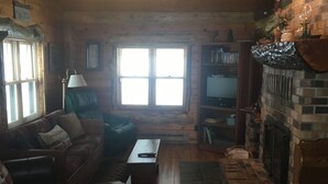 Een gezellig chaletinterieur met een houten vloer, een open haard, een bank en een televisie.