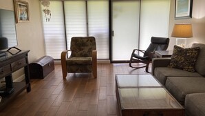 A living room with a wooden floor, a floral armchair, a sofa, a coffee table, a TV, and a lamp.
